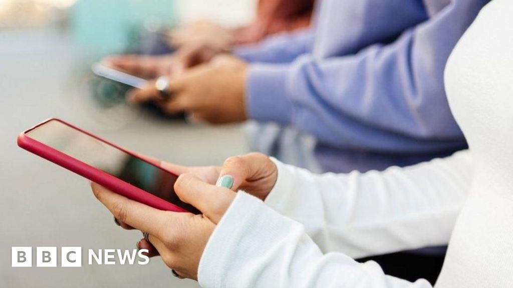A close-up image of several young people using smartphones that appears to be indoor. The background is softly blurred, emphasising the hands and devices in the foreground.