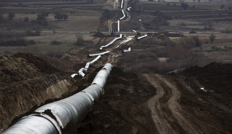 Welded gas pipe sections sit before laying beside a trench.
