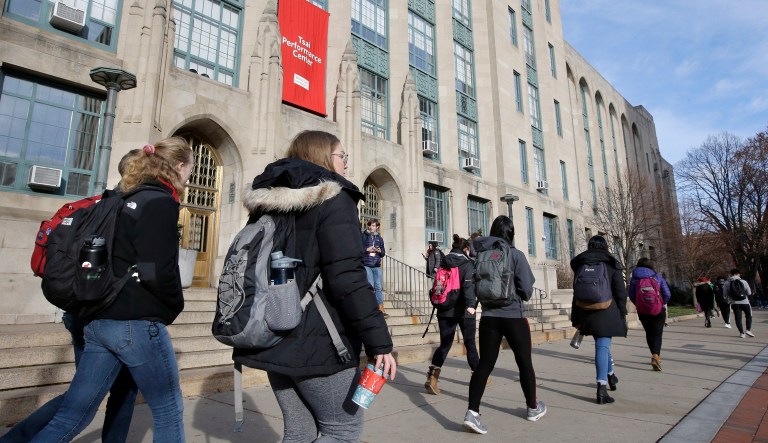 Students and passersby carry backpacks as they walk past an entrance to Boston University College of Arts and Sciences.