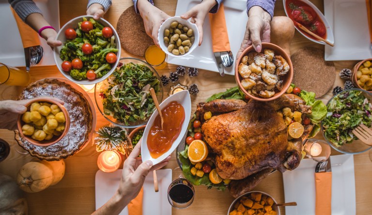 People passing side dishes during Thanksgiving dinner at dining table.