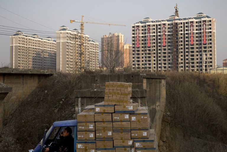 FILE - In this Monday, Jan. 20, 2014, file photo, a man talks on a mobile phone inside his tricycle cart loaded with goods near under-construction residential buildings in Changsha, in China's Hunan province. U.S. investors are being hit with new worries from overseas just as the economy at home appears to be strengthening. (AP Photo/Andy Wong, File)