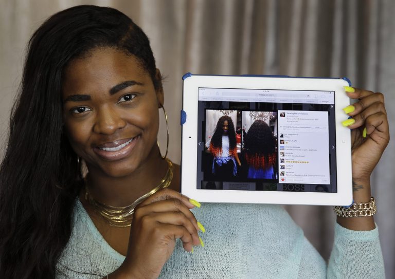 Miranda Jade Plater, owner of Limelight Extensions, poses with a tablet showing an Instagram photo of her wearing long, black curly hair extensions with the ends dyed bright orange at her salon in Farmington Hills, Mich. on Wednesday, June 18, 2014. This photo alone has generated about $10,000 in sales. (AP Photo/Paul Sancya)