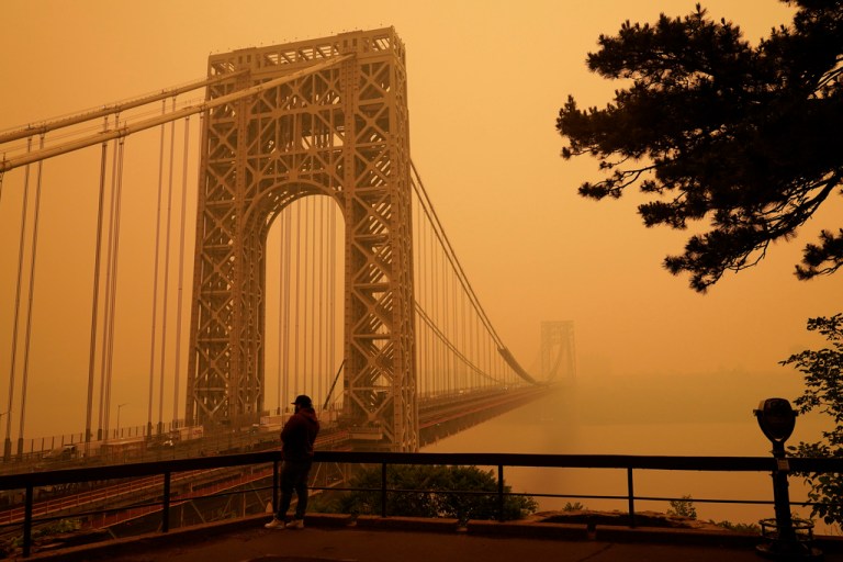 A man talks on his phone as he looks through the haze at the George Washington Bridge in Fort Lee, N.J., Wednesday, June 7, 2023.