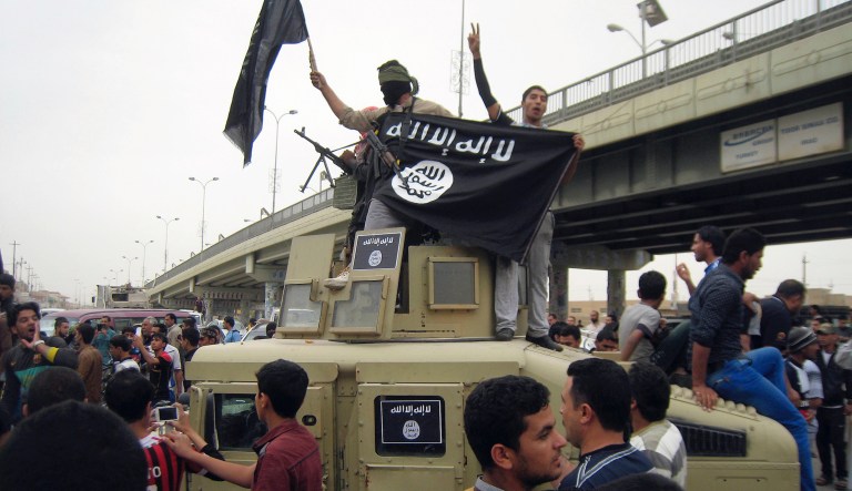 FILE - In this Sunday, March 30, 2014, file photo, Islamic State group militants hold up their flag as they patrol in a commandeered Iraqi military vehicle in Fallujah, 40 miles (65 kilometers) west of Baghdad, Iraq.