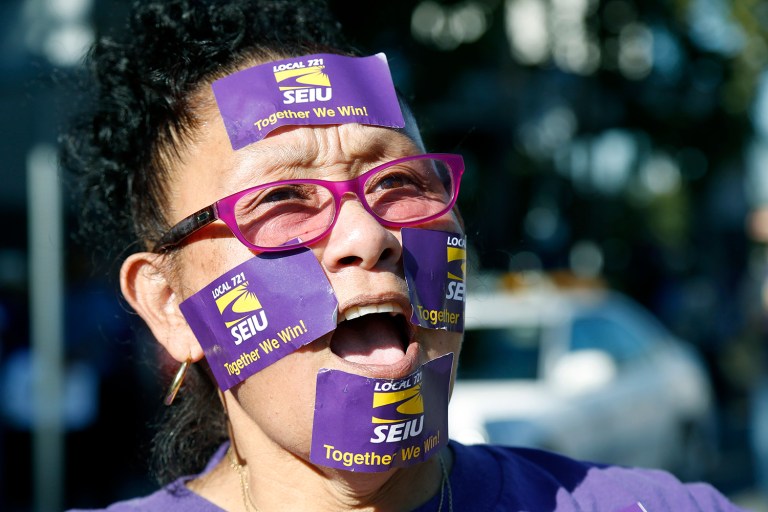 A woman shouts with purple SEIU stickers on her face.