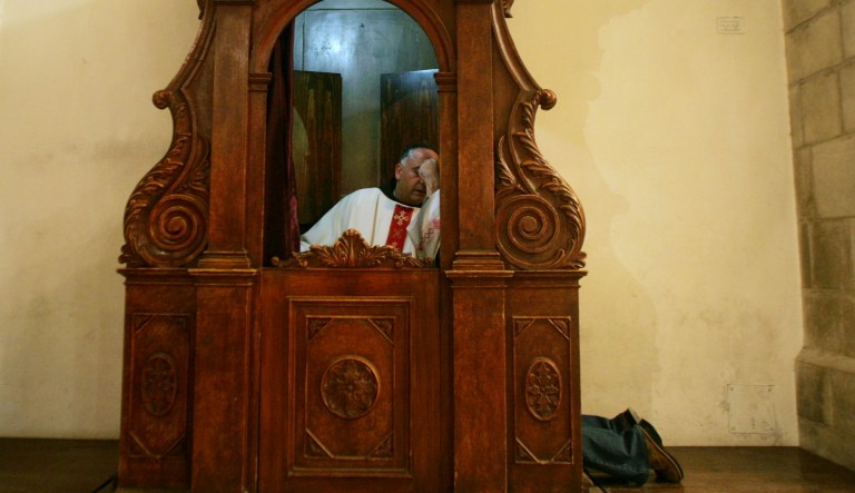 A Roman Catholic priest listens to a woman's confession as she kneels at right inside the St. Catherine's Church within the Church of the Nativity in the West Bank town of Bethlehem.