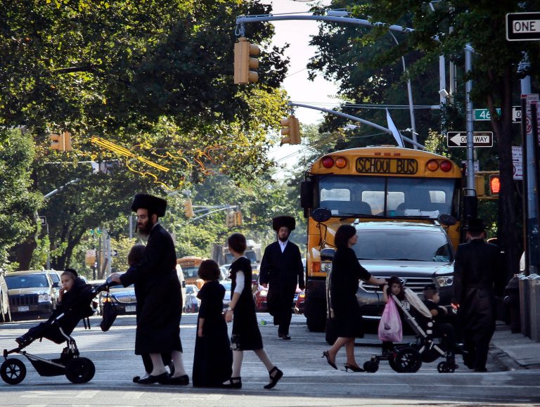 Children and adults cross a street in front of a school bus in Borough Park, a neighborhood in the Brooklyn borough of New York that is home to many ultra-Orthodox Jewish families. 