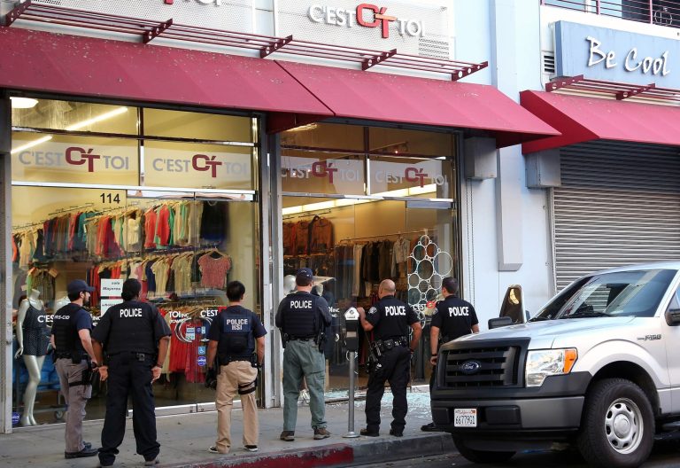 FILE - In this Wednesday, Sept. 10, 2014 file photo, law enforcement agents stand outside a clothing store after a raid in the Los Angeles Fashion District. Federal authorities on Thursday, Oct. 2, 2014, slapped new financial reporting rules on 2,000 businesses in the fashion district of Los Angeles in an effort to curtail suspected Mexican drug money laundering.(AP Photo/ Nick Ut, File)