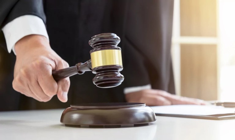 Close up of a lawyer or judge's hand striking the gavel on a sounding block.