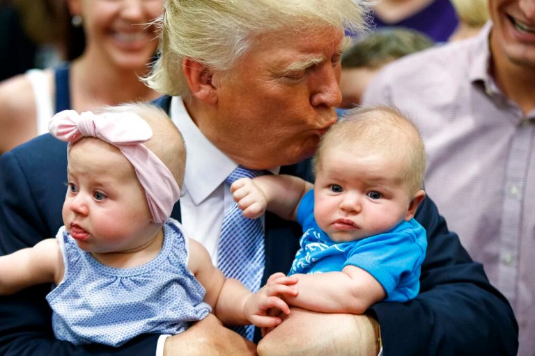 trump holding two babies, kissing one.