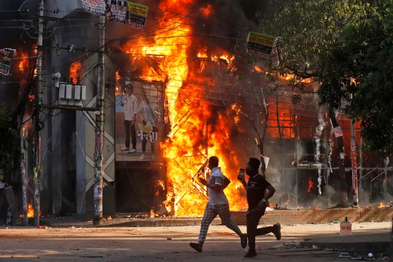 Men run past a shopping center which was set on fire by protesters during a rally against Prime Minister Sheikh Hasina and her government demanding justice for the victims killed in the recent countrywide deadly clashes