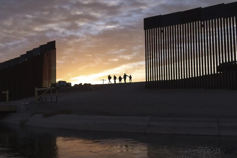 A pair of migrant families from Brazil passes through a gap in the border wall to reach the United States.