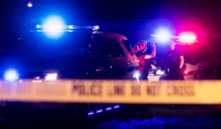 Police officers standing in background by car while blurry police tape is in the foreground.