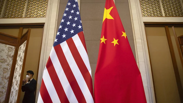 A staff member wearing a face mask walks past United States and Chinese flags.