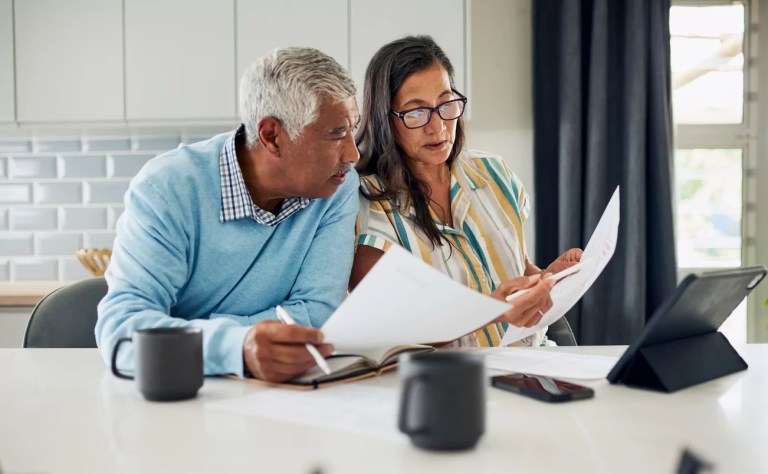 A couple is sitting at their kitchen table reviewing financial documents.