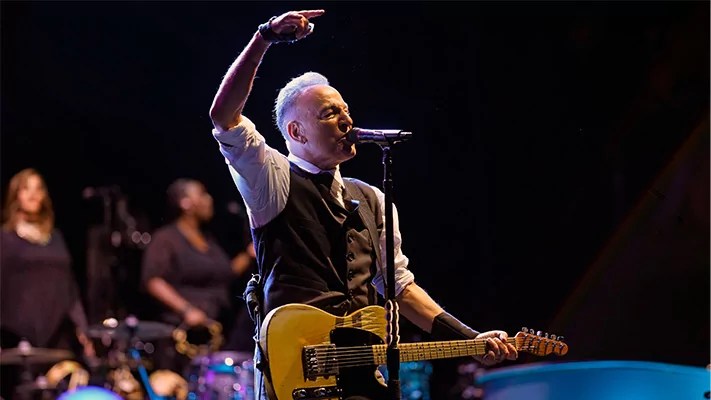 Bruce Springsteen on stage with guitar in hand and other arm up