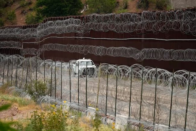 A vehicle drives along the U.S. side of the U.S.-Mexico border wall.