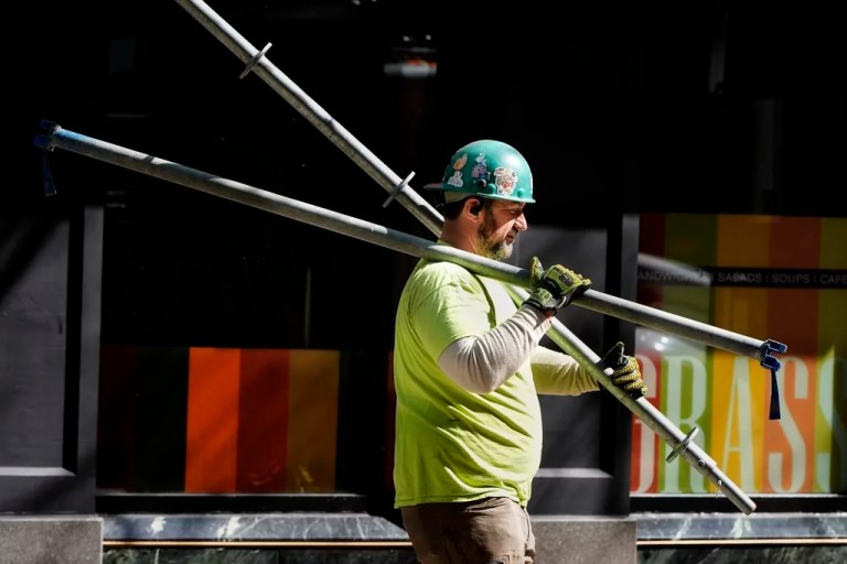 A construction worker carries scaffolding parts.