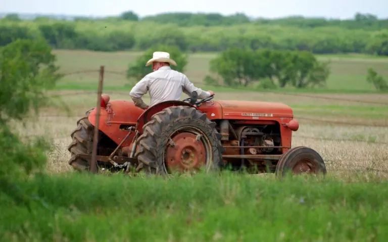 Charles Ray Gibbs drives an old tractor along a fence at Gibbs Farm in 2024.