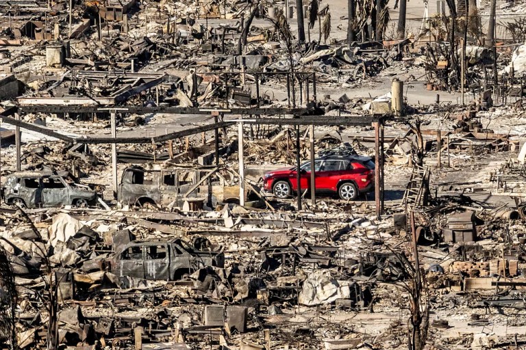 A car drives past homes and vehicles destroyed by the Palisades fire