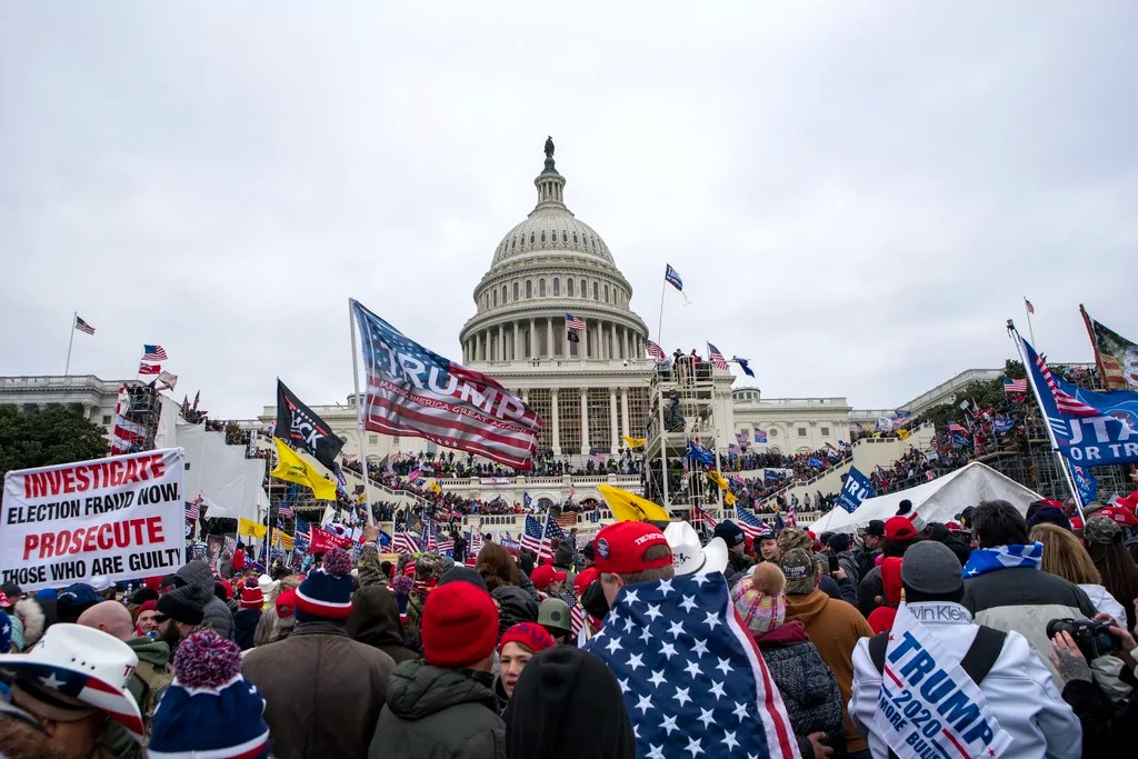 rioters stand outside the U.S. Capitol with Trump flags and signs on Jan. 6, 2021.