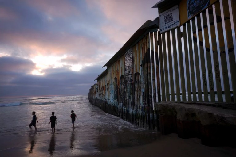 Three children play at the U.S.-Mexico border wall.