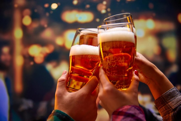 Hands clink glasses of beer together at a bar.