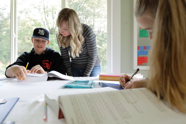 A mother works on a homeschool lesson with her son while her daughter works next to them in their home.