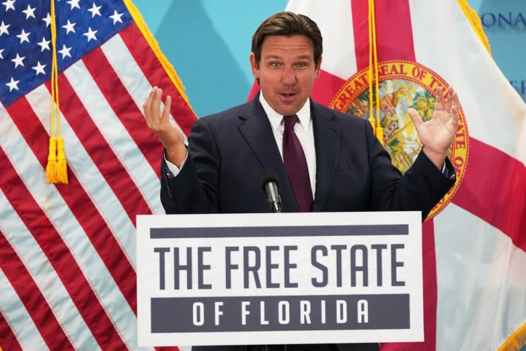 Florida Gov. Ron DeSantis speaks before a podium with the sign 