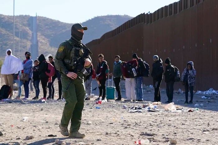 A member of Customs and Border Protection walks past a group of migrants.