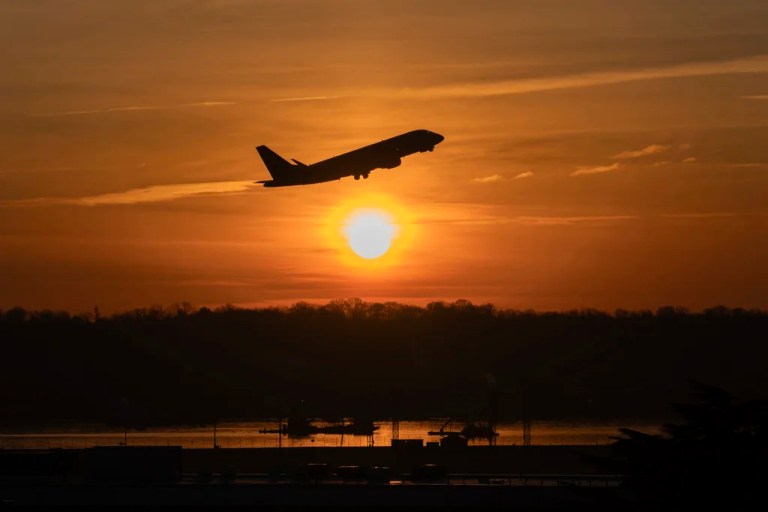 The sun rises as a jet lifts off above a wreckage site in the Potomac River.
