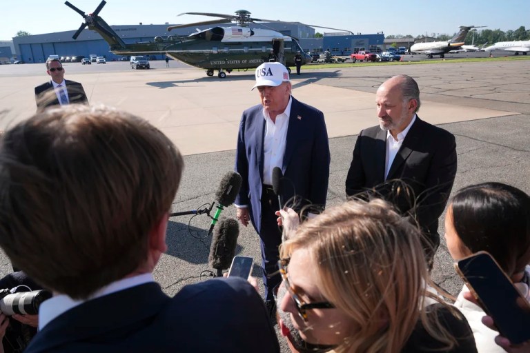 President Donald Trump, left, speaks with reporters as Commerce Secretary Howard Lutnick listens after arriving on Marine One, in background, and before boarding Air Force One at Morristown Municipal Airport in Morristown, New Jersey, Sunday, July 6, 2025, en route to Washington.