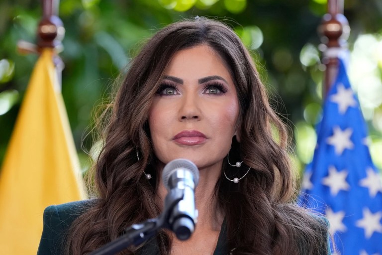 Kristi Noem stands in front of a flag from Ecuador and the United States as she speaks into a microphone