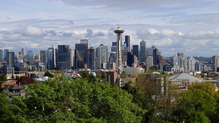 The Space Needle and the Seattle skyline are shown against a cloudy sky.