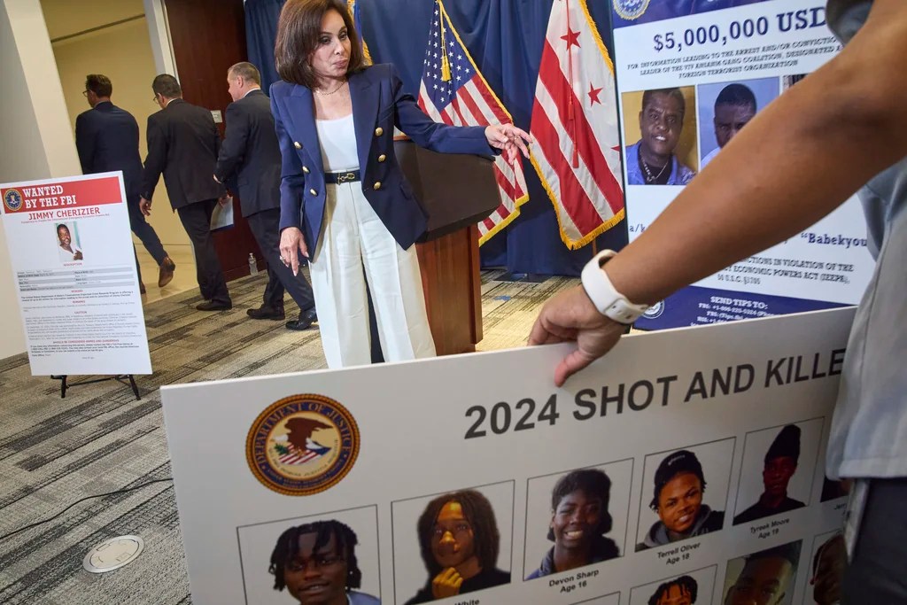 D.C. U.S. Attorney Jeanine Pirro gestures toward an unknown person holding a poster depicting people murdered in Washington in 2024.
