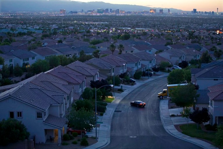 In this Wednesday, May 29, 2013, photo, the Las Vegas skyline glows at dusk as a motorist pulls into the driveway of a home, in Henderson, Nev. Home prices in the Las Vegas area are setting monthly records, according to an industry survey putting the median price of existing single-family houses at $375,000 in April. A report released Thursday, May 6, 2021, by the organization Las Vegas Realtors said local home prices have never been higher and the housing supply has rarely, if ever, been tighter. (AP Photo/Julie Jacobson, File)