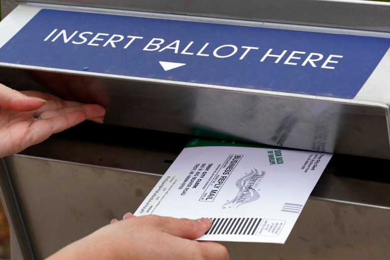 Nikki Schueller inserts her absentee voter ballot into a drop box.