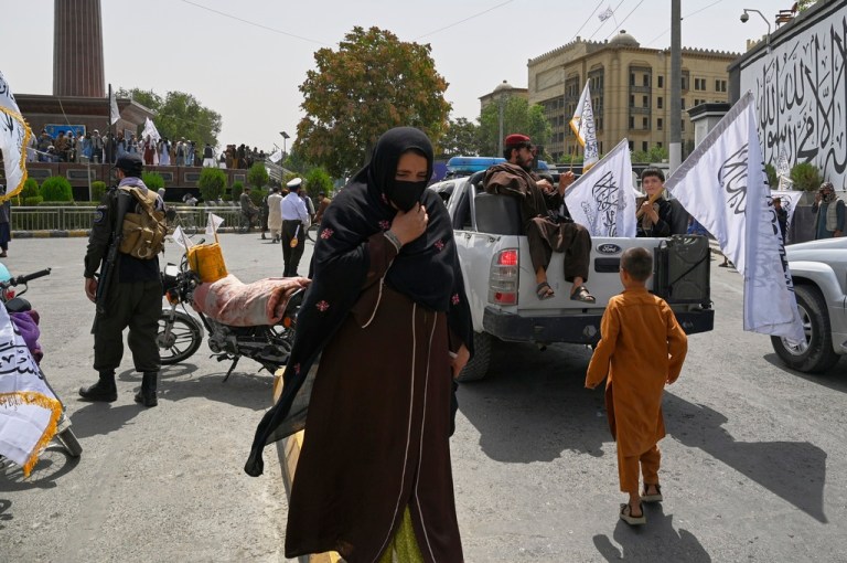 A woman wearing a face mask walks quickly through crowds of Taliban fighters and supporters during celebrations marking the fourth anniversary of the U.S. withdrawal and the start of Taliban rule in Kabul, Afghanistan, Friday, Aug. 15, 2025.