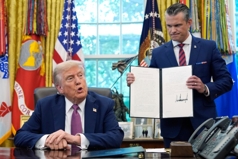 President Donald Trump speaks as Defense Secretary Pete Hegseth holds a signed executive order.