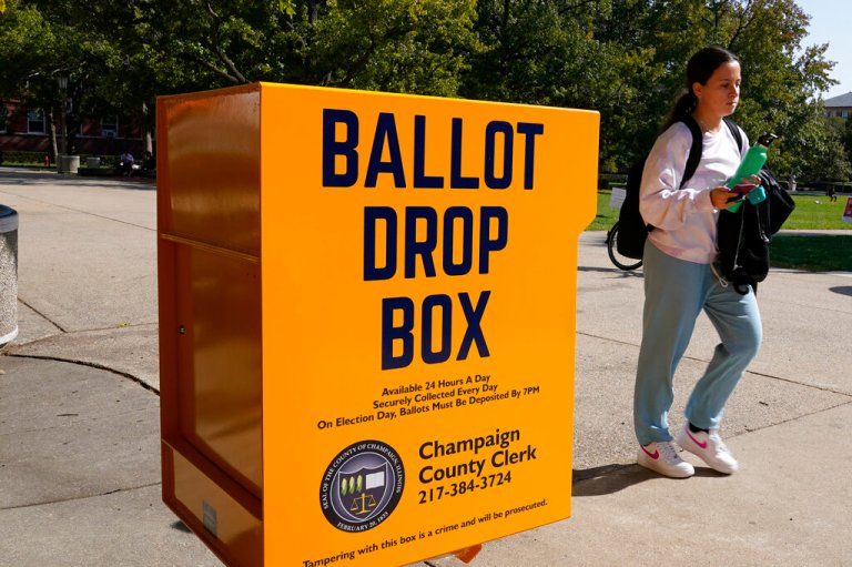 A University of Illinois student Tuesday, Oct. 6, 2020, walk past a mail-in ballot drop box that sits on the northwest corner of the university's Quad in Urbana, Ill. The new drop box option was authorized as part of a new state law signed by Gov. J.B. Pritzker in June to expand early voting options and help reduce the number of people who would otherwise vote in person in the midst of the COVID-19 pandemic.