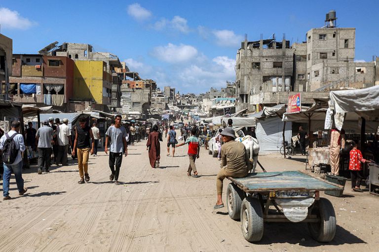 People walk past damaged buildings along a street in Khan Yunis in the southern Gaza Strip on September 30, 2025. Hamas was reviewing Donald Trump's plan for Gaza on September 30, while the Israeli prime minister said the military would stay in most of the territory after he gave the US president his backing. The plan calls for a ceasefire, release of hostages by Hamas within 72 hours, disarmament of Hamas and gradual Israeli withdrawal from Gaza, followed by a post-war transitional authority headed by Trump himself. (Photo by Omar AL-QATTAA / AFP) (Photo by OMAR AL-QATTAA/AFP via Getty Images)