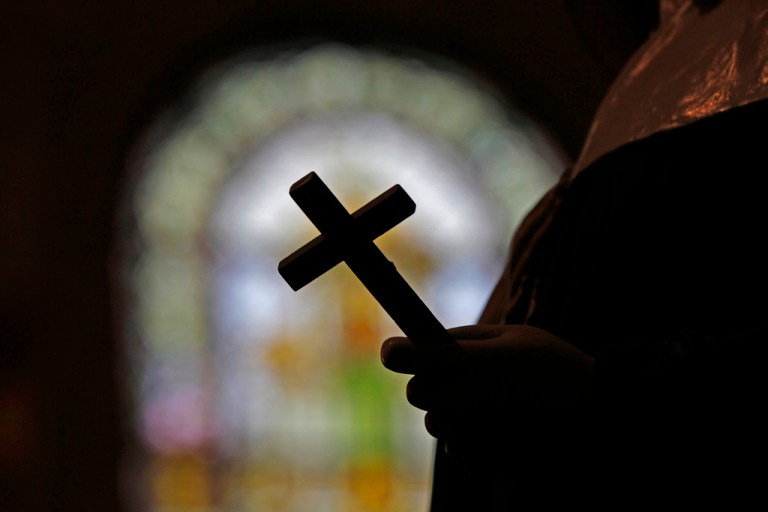 A crucifix is silhouetted in front of a stained glass window.