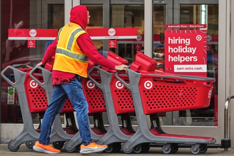 Signs for holiday hiring hang on the doors of a Target as an employee pushes carts.