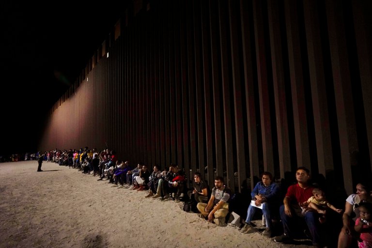 Migrants wait along a border wall after crossing from Mexico.