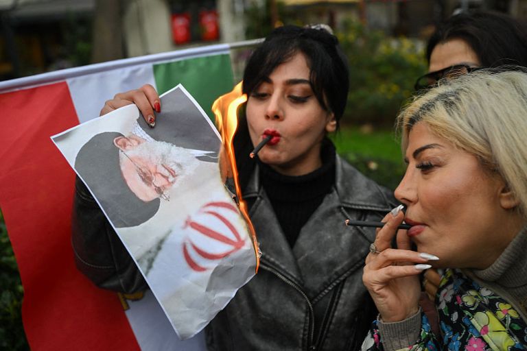 A woman burns a portrait of Iran's Supreme Leader, Ayatollah Ali Khamenei after lighting a cigarette.