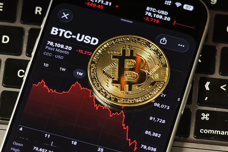 In this photo illustration, a Bitcoin coin is placed on a smartphone displaying the BTC-USD price chart showing a sharp decline, on February 4, 2026, in Chongqing, China. Bitcoin fell to its lowest level since U.S. President Donald Trump returned to office, dropping below the $75,000 mark amid sustained selling pressure, as traders grew more cautious toward risk assets and options markets signaled limited appetite for a rebound, according to recent market data. (Photo illustration by Cheng Xin/Getty Images)