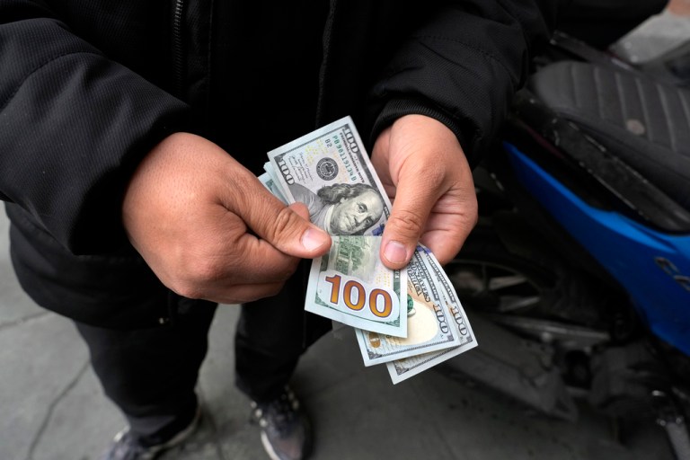 A street money exchanger holding $100 bills.