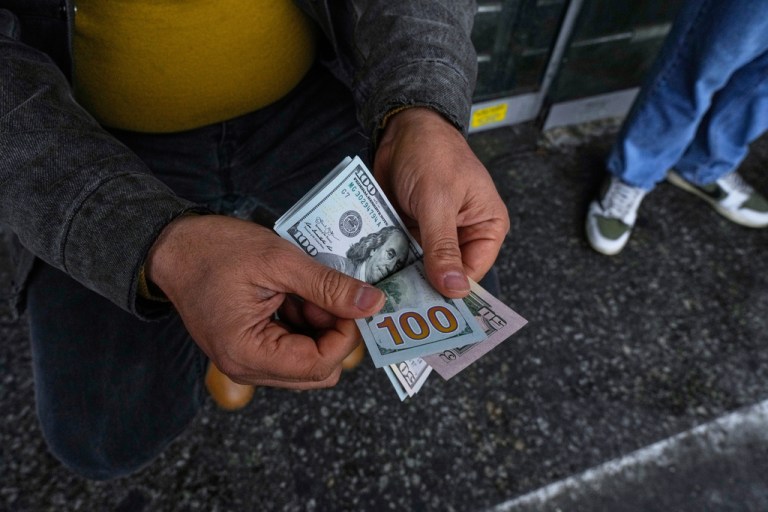 A street money exchanger poses for a photo without showing his face as he counts U.S. dollars.