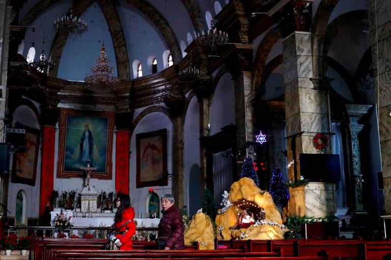 Chinese women walk past a decoration displaying a Baby Jesus doll part of a Nativity scene.
