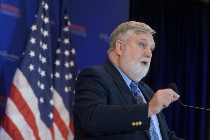 Douglas Wilson speaks in front of a pair of American flags